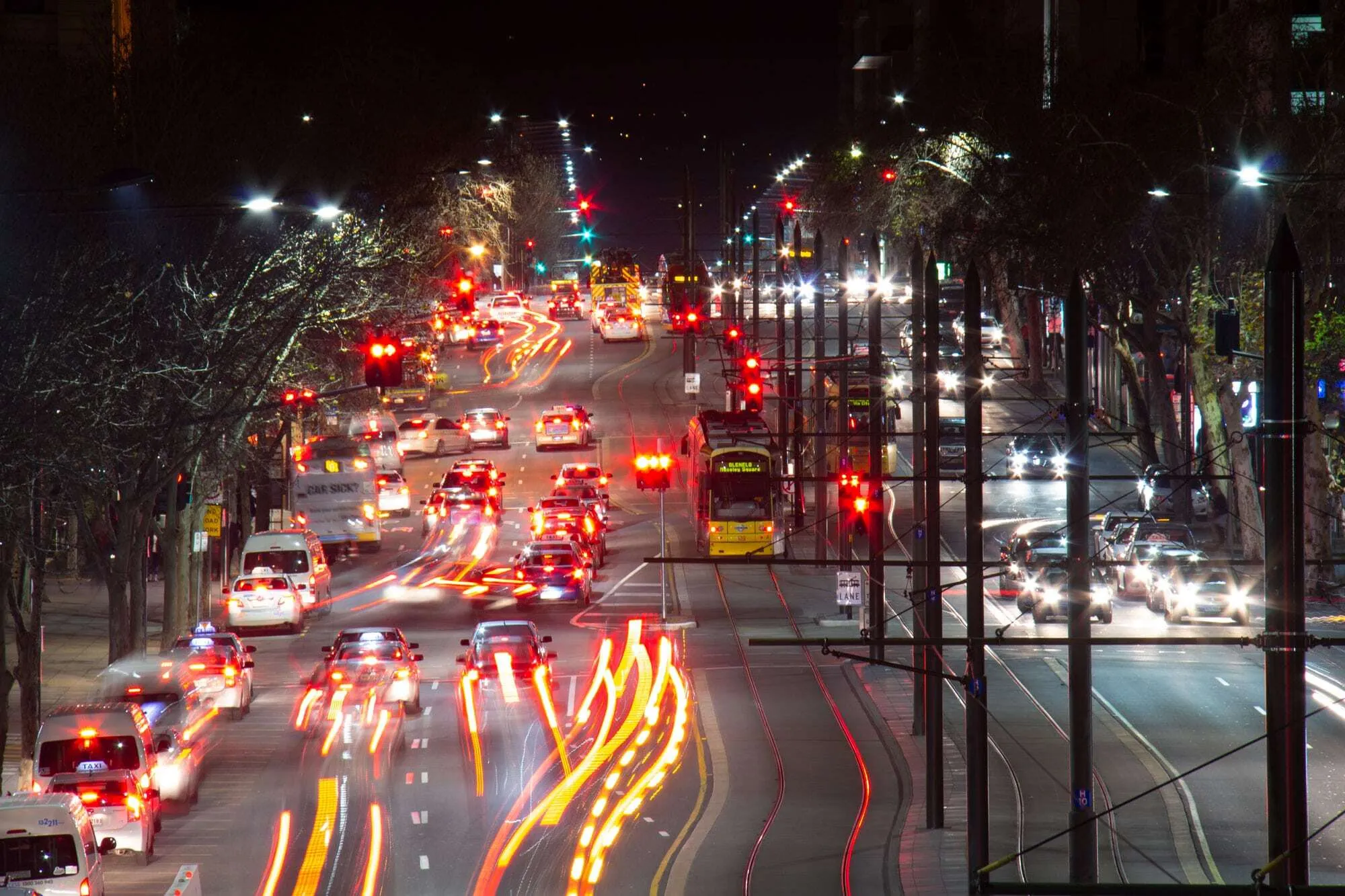 A long exposure photo of a busy road with cars and a tram at night